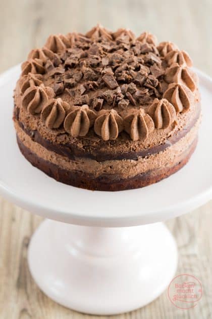 Schoko-Brownie-Torte mit Schokocreme-Tupfen und Schokosplittern auf weißem Tortenständer