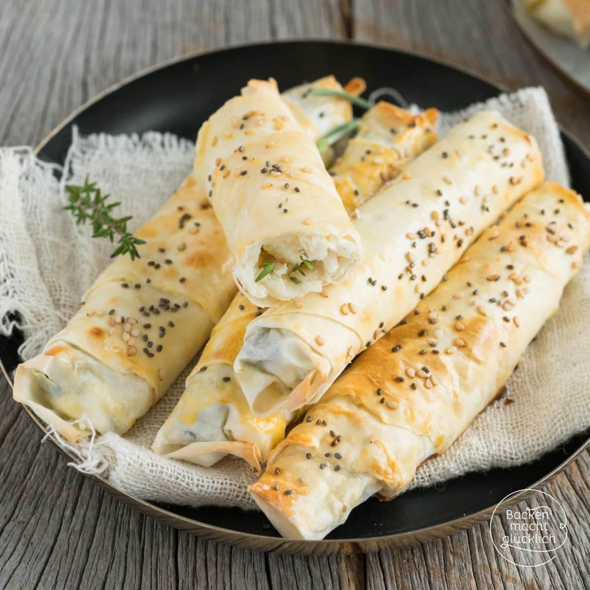 Gerollte Börek mit Schafskäse und Spinat, angeschnitten auf schwarzem Teller mit Thymian