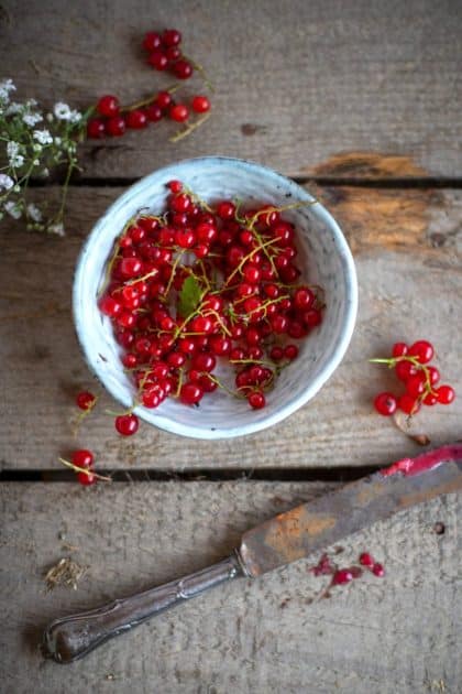Rote Johannisbeeren mit Rispen in weißer Schale auf Holztisch