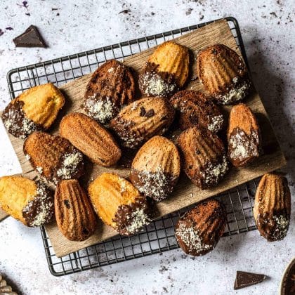 Madeleines, teils in Schokolade getaucht, auf Holzbrett und Kuchengitter