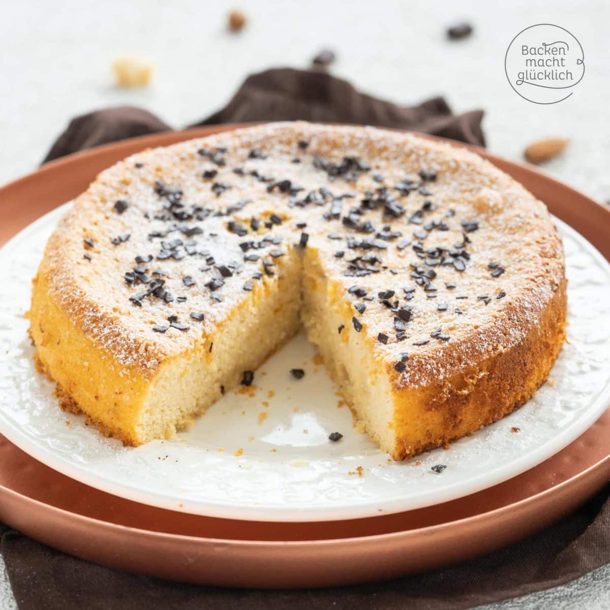 Angeschnittener Marzipankuchen mit Puderzucker und Schokostreuseln auf weißem Teller