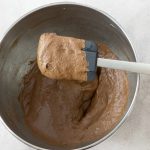 Schokoladenmasse wird mit Silikonspatel in Metallschüssel glattgestrichen