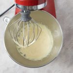Flüssige Eier-Zucker-Masse wird mit Küchenmaschine in Metallschüssel schaumig geschlagen