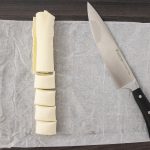 In Scheiben geschnittene Butterrolle neben Kochmesser auf Backpapier