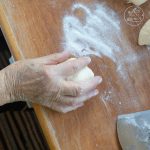 Hand formt Teigkugel auf bemehlter Holzarbeitsfläche mit Teigkarte
