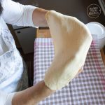 Hände ziehen dünnen Strudelteig über kariertem Tuch