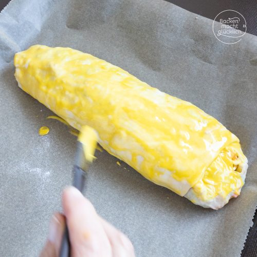 Ungebackener Strudel wird auf Backpapier mit Eigelb bestrichen