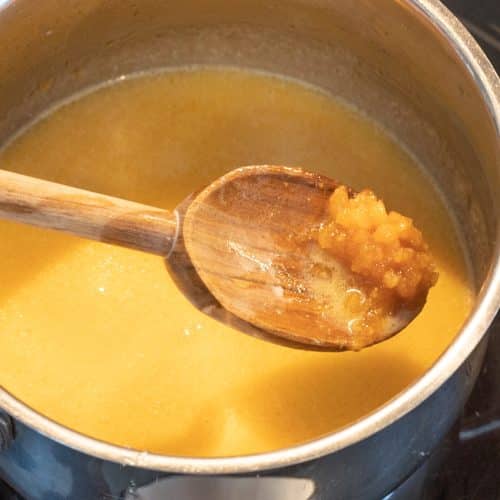 Karamellsauce köchelt im Topf, Holzlöffel mit angedickter Karamellcreme darüber