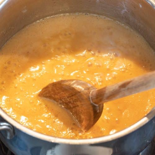 Karamellmasse köchelt blubbernd im Topf, wird mit Holzlöffel gerührt