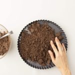 Hand drückt Lebkuchenkrümel in gerippte Tarteform, Schüssel mit Krümeln daneben