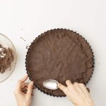 Kekskrümelboden wird mit Löffel in Tarteform gedrückt und geglättet