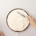 Hand streicht Cremefüllung mit Palette in Schokoladentarteboden