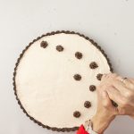 Schokoladentupfen werden auf Frischkäse-Tarte mit Keksboden gespritzt