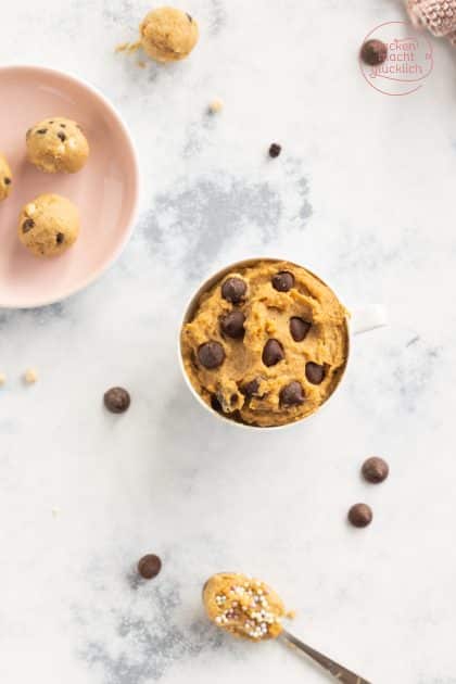Cookie Dough aus Kichererbsen in Tasse mit Schokotropfen, Kugeln auf rosa Teller