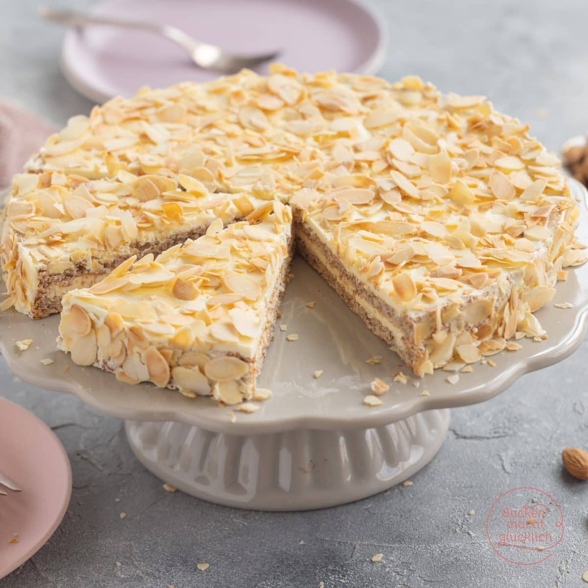 Angeschnittene Mandeltorte mit Sahnefüllung, dicht mit Mandelblättchen bedeckt, auf Tortenständer