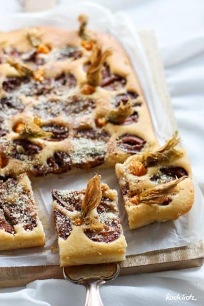 Pflaumenkuchen mit Physalis, angeschnitten in Stücke auf Backpapier