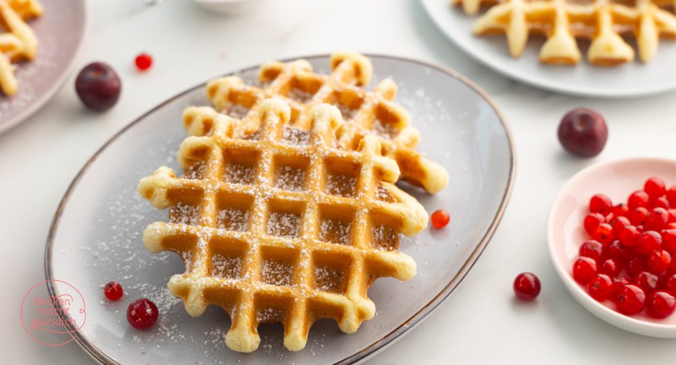 Waffel mit Puderzucker bestäubt, daneben Johannisbeeren und Kirschen