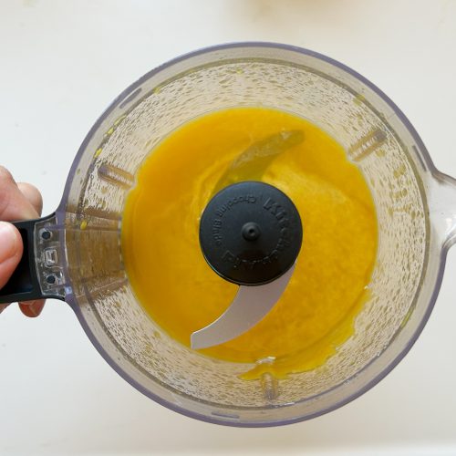 Küchenmaschine mit pürierter gelber Masse und Hackmesser von oben
