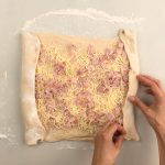 Teigränder werden über Käse-Schinken-Füllung auf bemehlter Arbeitsfläche gefaltet