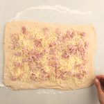 Ausgerollter Hefeteig mit geriebenem Käse und Schinkenwürfeln auf Arbeitsfläche