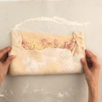 Hände falten Hefeteig über Käse-Schinken-Füllung auf bemehlter Arbeitsfläche