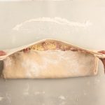 Hände rollen Teig mit Käse-Schinken-Füllung zu Handbrot auf
