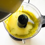 Flüssigkeit wird in Küchenmaschine mit gelb-grüner Pistaziencreme gegossen