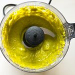 Gelbgrüne Pistaziencreme im Küchenmaschinenbehälter mit Zerkleinerungsklinge