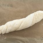 Gedrehter Brotteigstrang auf bemehltem Backpapier vor dem Backen