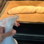 Geflochtenes Wurzelbrot auf Backblech wird vor dem Backen mit Wasser besprüht