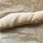 Rustikales Wurzelbrot mit gedrehter Form auf Backpapier, mehlbestäubte Kruste