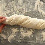 Hand verdreht Brotteig zu Wurzelbrot auf bemehlter Arbeitsfläche