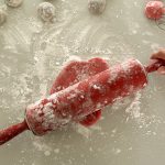 Roter Mochi-Teig wird mit bemehltem Nudelholz auf mehliger Arbeitsfläche ausgerollt
