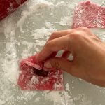 Rote Mochi-Teigplatte wird um Füllung herum zu Kissen gefaltet