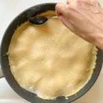 Mürbeteig wird mit Löffel in Pfanne für Tarte Tatin glattgestrichen