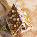 Lebkuchenhaus mit bunten Bonbons, Zuckerguss und Lebkuchenmann auf Holzbrett
