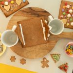 Lebkuchenhauswände zwischen Tassen gestützt, umgeben von Lebkuchenfiguren und Smarties