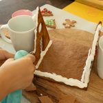 Lebkuchenhauswände mit Zuckerguss zusammenkleben, von Tassen gestützt