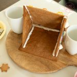 Lebkuchenhauswände mit Zuckerguss verklebt auf Holzbrett, Tassen daneben
