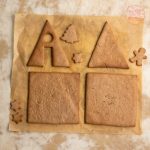 Gebackene Lebkuchenhaus-Teile mit Sternen und Tannenbaum auf Backpapier