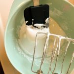 Steif geschlagenes Eiweiß an Mixer und Teigschaber in grüner Rührschüssel