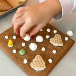 Hand verziert Lebkuchenwand mit Baisertupfen, Schokolinsen und Waffelherzen
