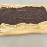 Ausgerollter Hefeteig mit Mohnfüllung wird zur Rolle eingeschlagen