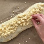 Hand streut Streusel auf Hefeteigstrang mit Mohnfüllung