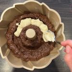 Helle Frischkäsecreme wird löffelweise auf Kakaoteig in Gugelhupfform gegeben