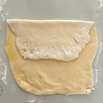 Ausgerollter Hefeteig zur Hälfte gefaltet auf bemehlter Arbeitsfläche