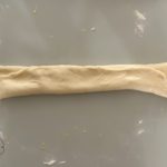 Zusammengerollter Hefeteig für Splitterbrötchen liegt auf bemehlter Arbeitsfläche