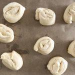 Ungebackene Splitterbrötchen aus gerolltem Hefeteig auf Backpapier