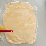 Ausgerollter Hefeteig wird mit Butter bestrichen, Backpinsel liegt daneben
