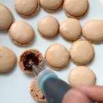 Schokoladencreme wird mit Spritzbeutel auf Macaron-Schalen gefüllt